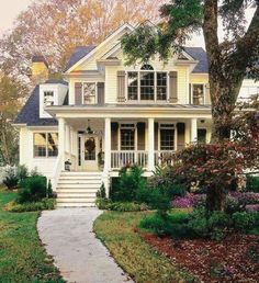 a white house with lots of trees and flowers in front of the porch, stairs leading up to the second floor