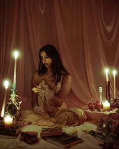 a woman sitting on a bed with candles in front of her and other items around her