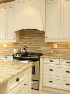 a kitchen with white cabinets and granite counter tops, an oven hood over the stove