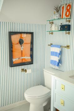 a bathroom with blue and white striped wallpaper, toilet and shelf above it is an orange life preserver