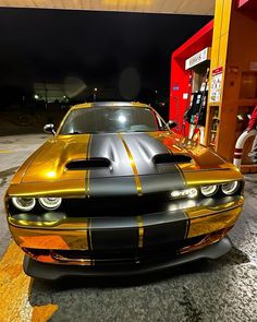 a gold and black car parked in front of a gas station at night with the lights on