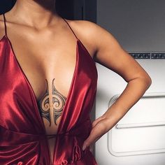 a woman in a red dress with tattoos on her chest and arms behind her back