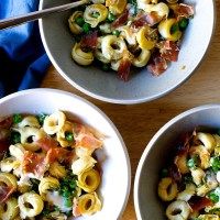 three bowls filled with pasta and vegetables on top of a wooden table next to chopsticks