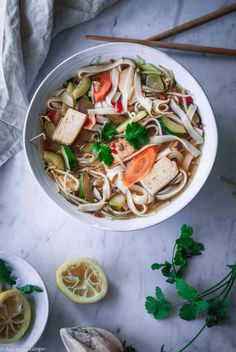 a white bowl filled with noodle soup next to sliced lemons and parsley