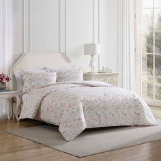 a white bed with pink flowers on it in a room next to a large window