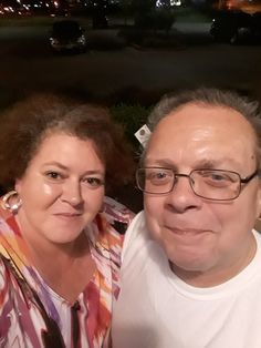 the man and woman are posing for a photo together outside at night with cars in the background