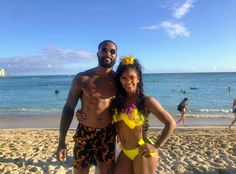 a man and woman posing for a photo on the beach with people in the background