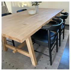 a wooden table with black chairs and a white vase on top of it in a room