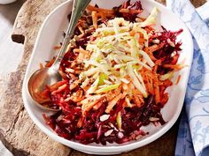 a white bowl filled with coleslaw and carrots on top of a wooden cutting board