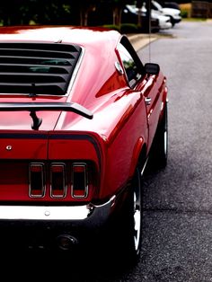 the rear end of a red car parked in a parking lot with other cars behind it