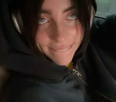 a woman wearing a black hoodie and smiling at the camera while sitting in a car