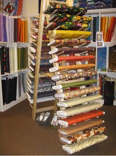 a rack full of different colored fabrics in a room filled with shelves and shelving