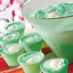 green jello with whipped cream in a bowl and six glasses lined up on a table