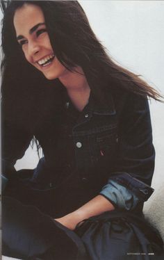 a woman sitting on the ground with her hair blowing in the wind and holding a purse