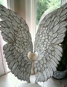 a large metal angel wings sitting on top of a tile floor next to a window