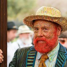 a man with a red beard wearing a straw hat and colorful suit is reflected in a mirror