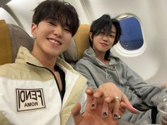 two people sitting on an airplane with their hands in the air and one person pointing at the camera