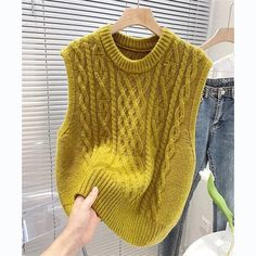 a person holding up a yellow sweater on a hanger next to some jeans and a window