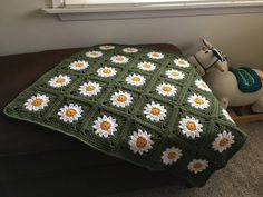 a crocheted blanket with daisies on it next to a toy horse and window