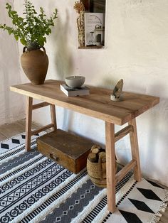 a wooden table sitting on top of a rug next to a vase and potted plant