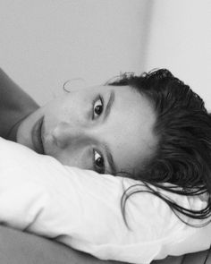 a black and white photo of a woman laying on a bed looking at the camera