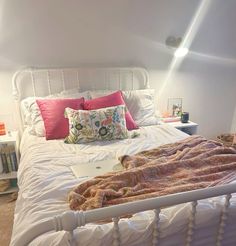 a white bed with pink pillows and blankets on it's headboard in a bedroom