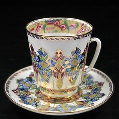 an ornate cup and saucer on a black surface with gold trimming, decorated with colorful