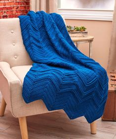 a blue blanket sitting on top of a white chair next to a brick wall in a living room