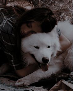 a woman laying on top of a bed next to a white dog with it's tongue hanging out