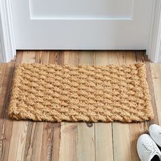 a pair of white shoes sitting on the floor next to a door mat that has been made out of jute