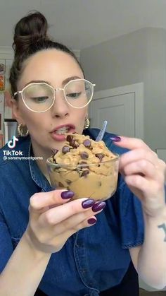 a woman wearing glasses eating a chocolate chip cookie