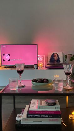 a table with books, glasses and a computer monitor on it in front of a pink light