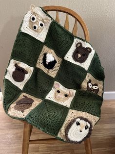 a crocheted blanket with animals on it sitting on a wooden chair in front of a wall