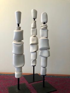 three tall white sculptures on black stands in front of a wall and carpeted floor