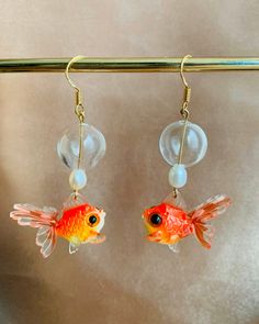 two goldfish earrings with pearls hanging from hooks