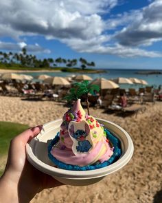 a person holding up a cupcake on the beach with a palm tree in it