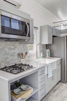 a white kitchen with stainless steel appliances and wood flooring, along with gray cabinets
