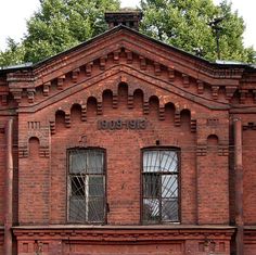 an old red brick building with windows and bars on the top, in front of some trees