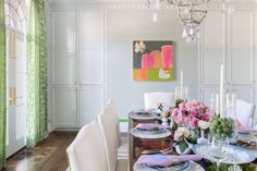 the dining room table is set with white chairs and pink flowers on top of it