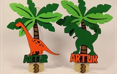 two paper cut out dinosaurs standing next to each other with palm trees in the background