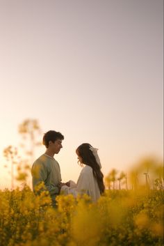 a man and woman standing in the middle of a field with yellow wildflowers