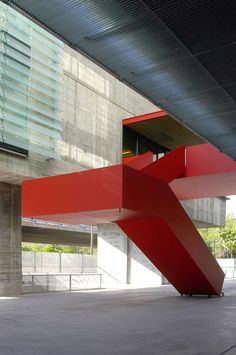 a large red object sitting in the middle of a walkway next to a tall building