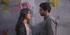 a man and woman standing next to each other in front of a wall with graffiti on it