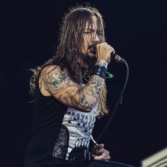 a man with long hair and tattoos on his arm holding a microphone in front of him