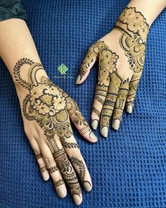 two hands with henna designs on them sitting on a blue surface next to each other
