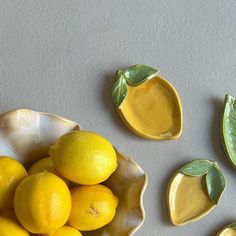 some lemons are sitting in a bowl next to other yellow fruits and leaf decorations