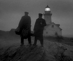 two men standing on top of a hill next to a lighthouse