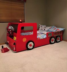 a red firetruck bed in a room with white carpet and brown wallpaper