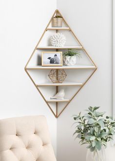 a white and gold shelf with some pictures on it next to a potted plant