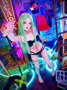 a woman with long green hair standing in front of a neon light filled building and pointing at the camera